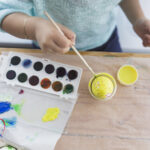 crop child painting egg with yellow