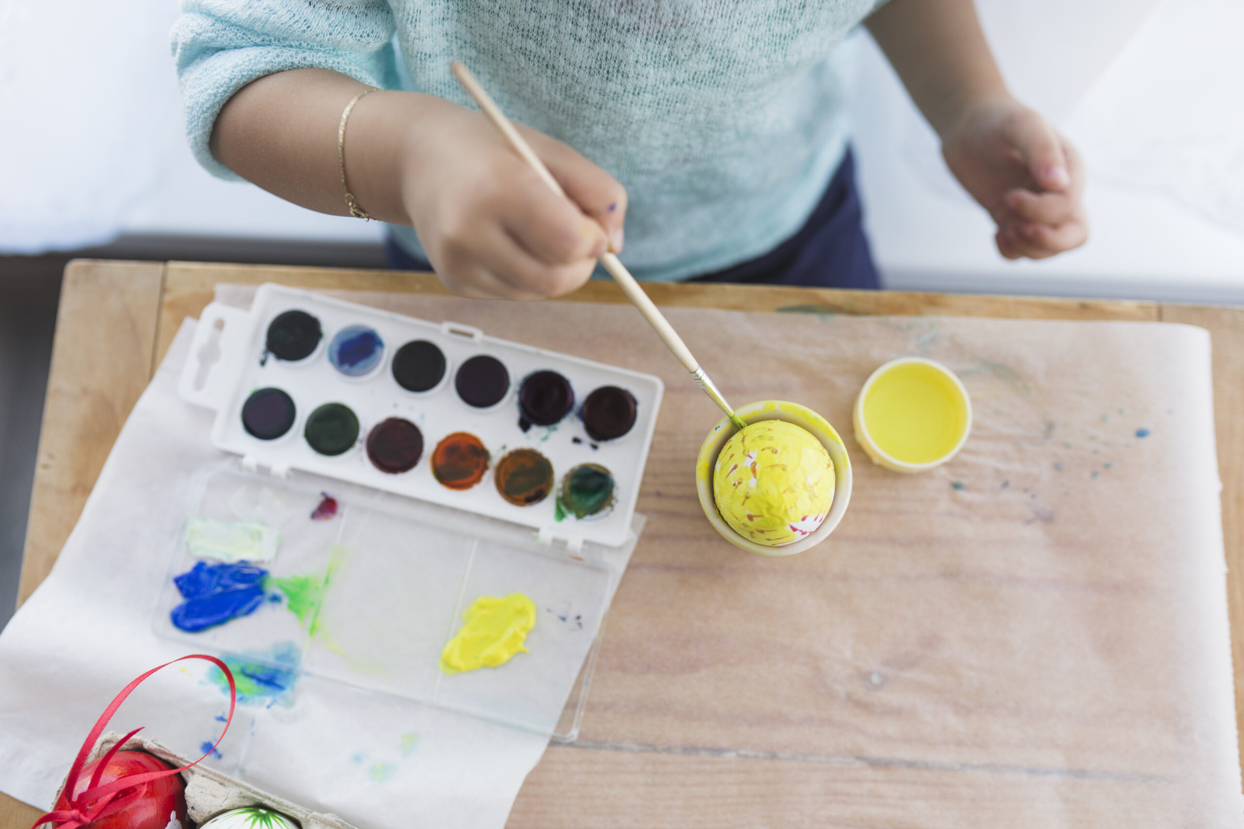 crop child painting egg with yellow